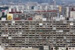 Aerial view of Petržalka residential district in Bratislava, Slovakia, showing rows of large Soviet-era prefabricated concrete apartment blocks (panelák) with hundreds of balconies displaying laundry, satellite dishes, and plants, with more housing towers and the city skyline visible in the background