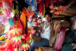 Two men seated inside a vibrantly decorated truck cab adorned with colourful artificial flowers, garlands and religious imagery, Rajasthan, India. Photograph by David Levene, 13 November 2010.