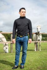 Silvestre De Sousa, Brazilian-born champion flat racing jockey, standing in a paddock field with thoroughbred horses, England. Photograph by David Levene, 27 August 2015