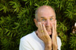 Russ Abbot, British comedian and entertainer, pulling a comic expression with his hands on his face against a green foliage background. London. Photograph by David Levene, 12 August 2026